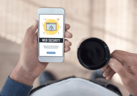 Man wearing blue sweater holding a cup of coffee and Web Security prompt on a cellphone with the other hand