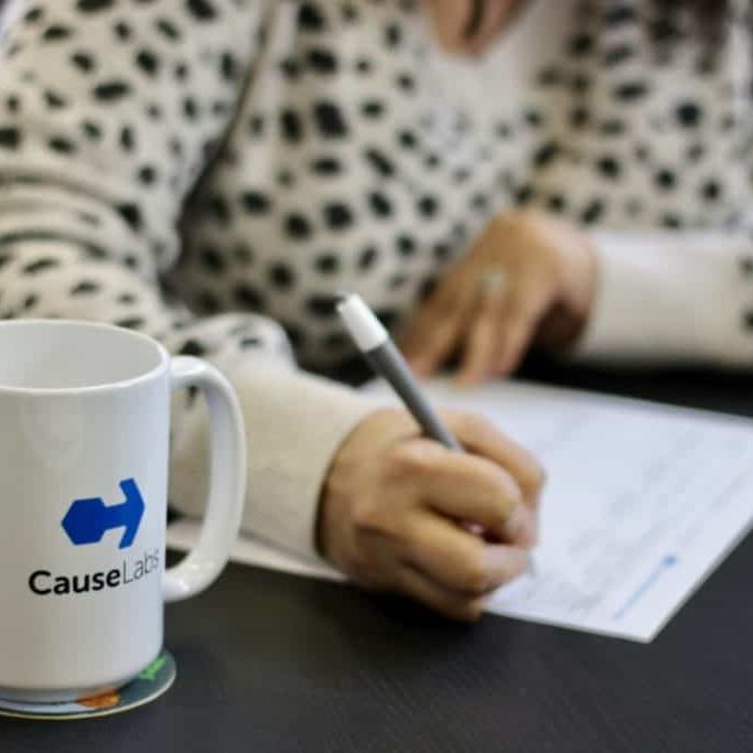 A person's hands writing and a CauseLabs coffee mug