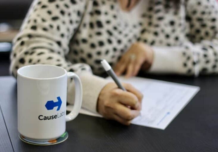 A person's hands writing and a CauseLabs coffee mug
