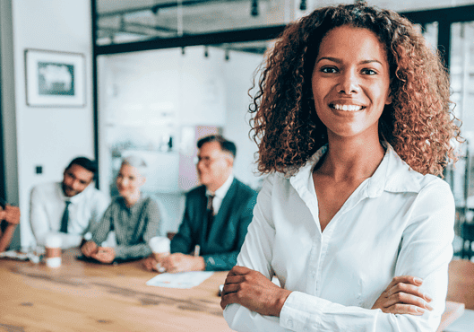 Woman of color with natural hair smiling in front of her team in office. An image for our risk management and risk mitigation post.