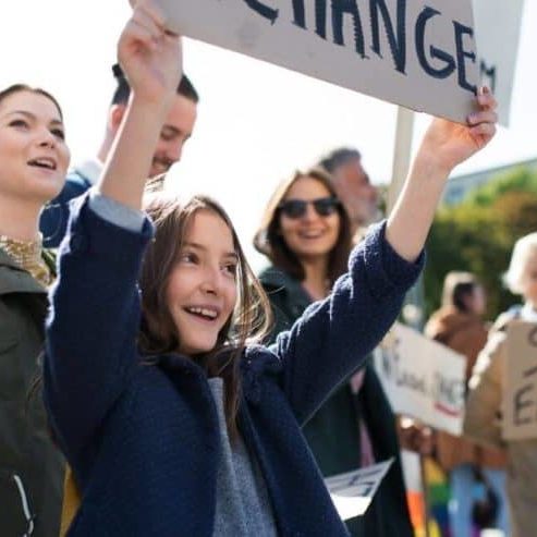 A young girl stands in a crowd holding a sign that says "change"