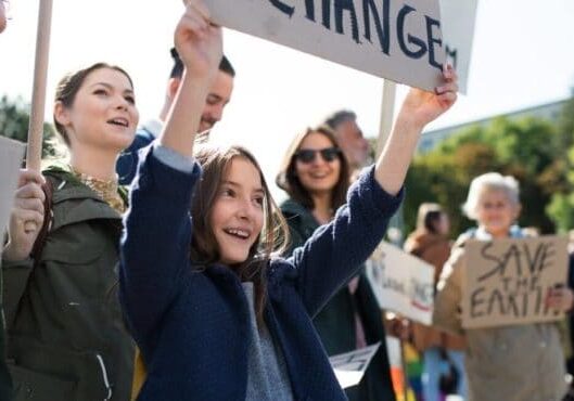 A young girl stands in a crowd holding a sign that says "change"