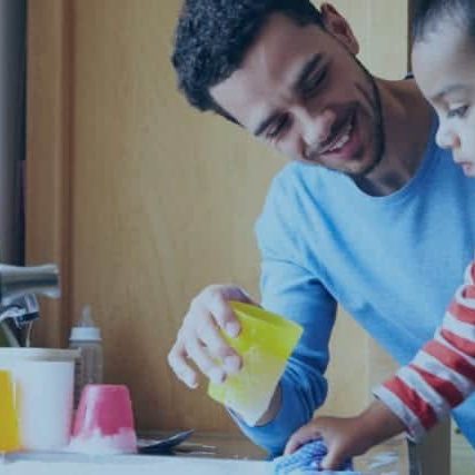 A father teach a young boy how to clean his cup in the sink.