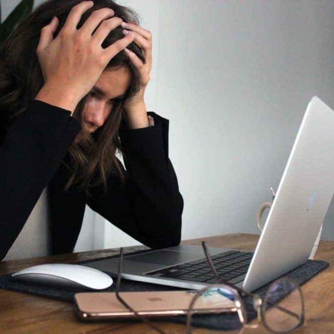 Woman looking at a laptop screen with her hands on her head in frustration