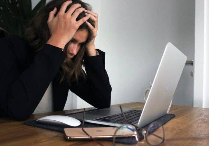 Woman looking at a laptop screen with her hands on her head in frustration