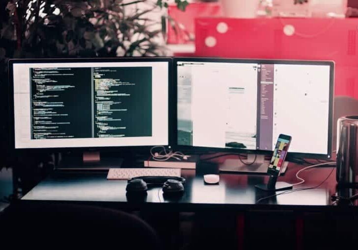 A desk with two monitors displaying code.