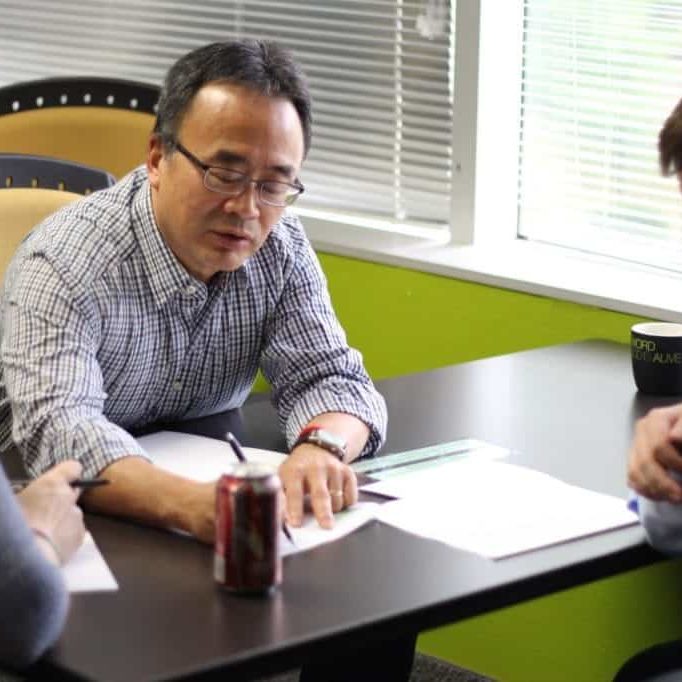 A man writing while conversing with two people during an HCD workshop