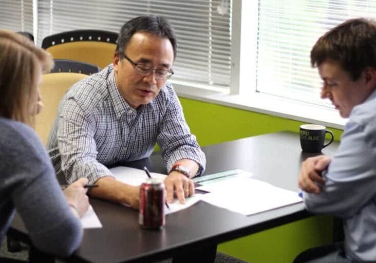 A man writing while conversing with two people during an HCD workshop