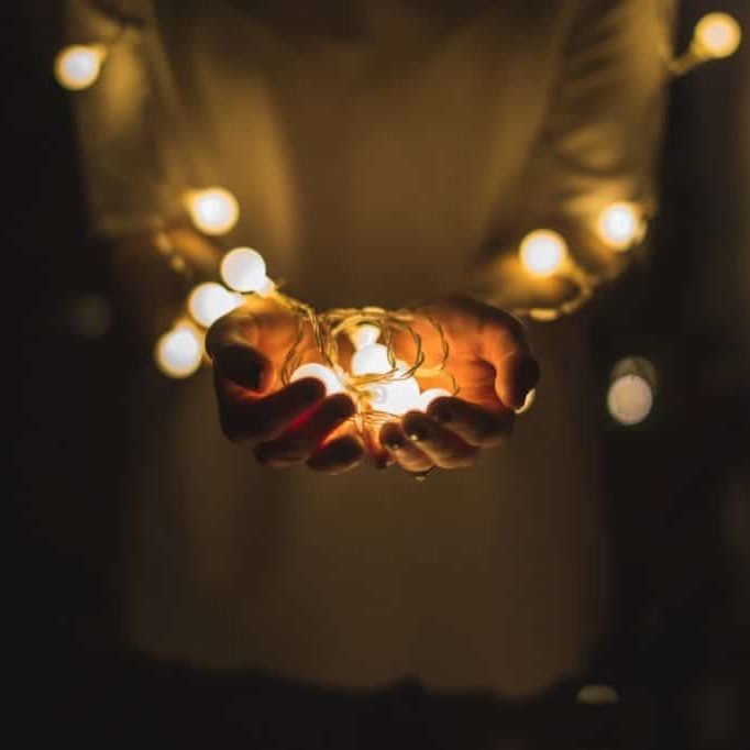A person holds a bundle of glowing holiday lights in their hands