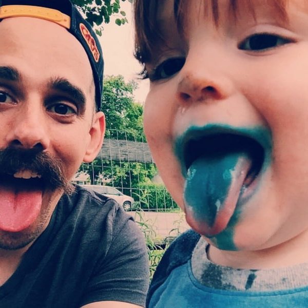 A man and child stick their tongues out. The child's tongue is blue from candy