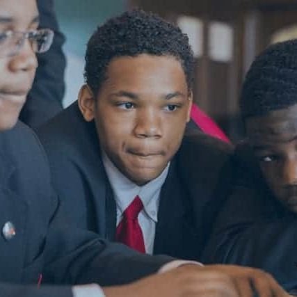 A group of students dressed in suits gather around a laptop