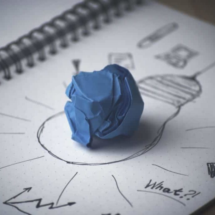 A crumpled sheet of blue paper sits on top of a pen and ink drawing of a lightbulb