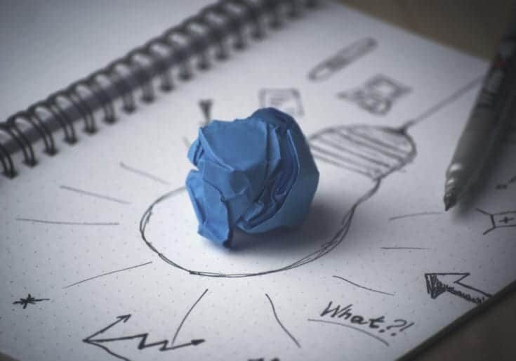 A crumpled sheet of blue paper sits on top of a pen and ink drawing of a lightbulb