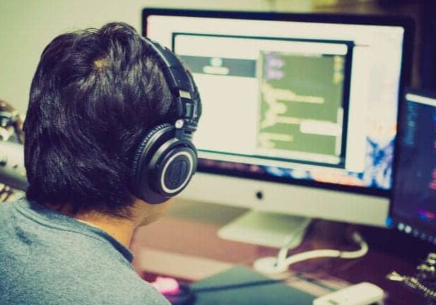 A man wearing headphones works at a computer station.