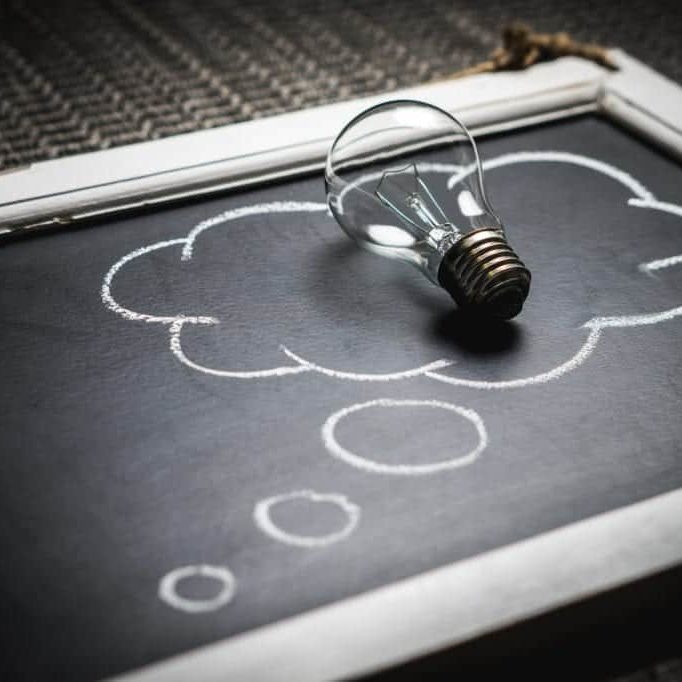 A small chalkboard with a thought bubble drawn on it and a lightbulb sitting on top of the bubble