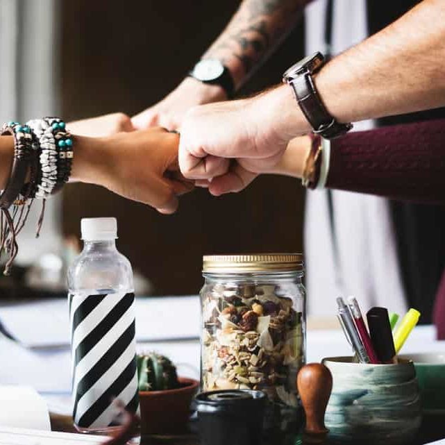 A closeup shot of a team of coworkers fist bumping.