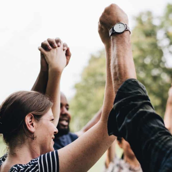 A diverse group of people holding hands in the air. A photo for our social impact post.